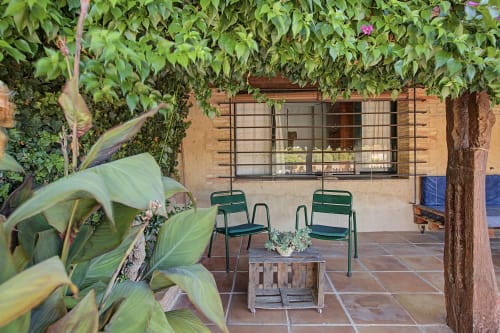 Patio rústico de Can Gat Vell con sillas verdes, baldosas de terracota, muros cubiertos de hiedra y vistas al jardín cerca de Costa Brava