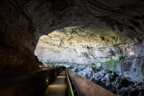 Illuminated underground cave passage with rock formations and wooden railing in Ariège, France