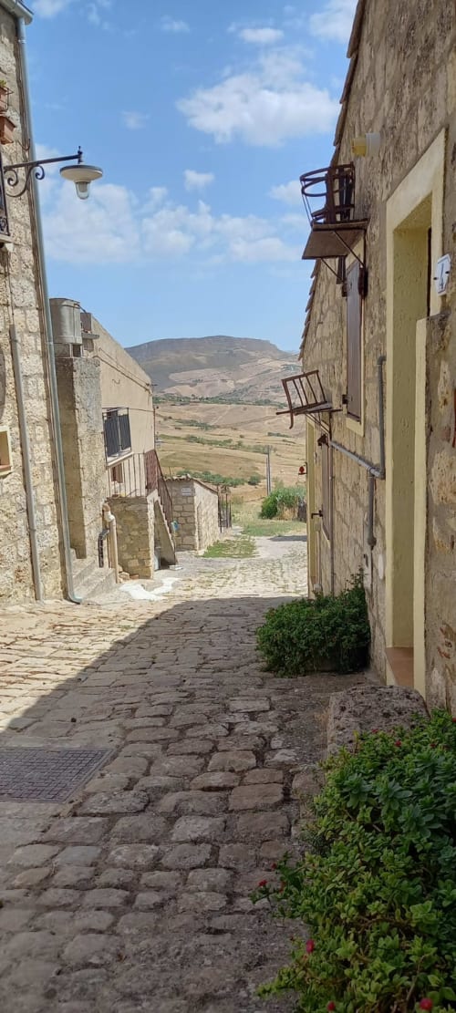 Stretto vicolo in ciottolato a Petralia Soprana con edifici in pietra e vista sulla valle montana, Case Vacanze Borgo i Stritti