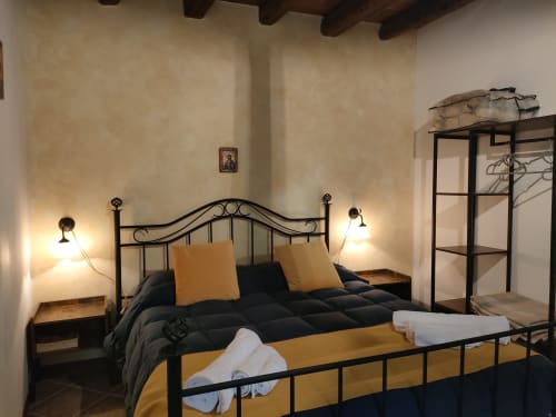 Camera rustica a Petralia Soprana con letto in ferro battuto, cuscini gialli, biancheria nera e illuminazione calda