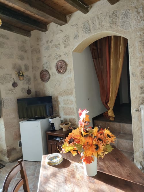 Interno soleggiato dell'appartamento a Case Vacanze Borgo i Stritti con muri in pietra, fiori autunnali, TV e porta ad arco