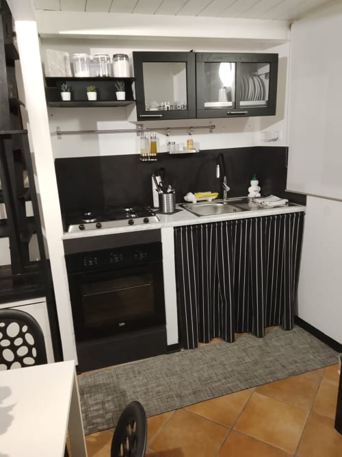 Kitchenette moderna in bianco e nero con piano cottura a gas, forno e mobili contenitori in Appartamento Bianco a Case