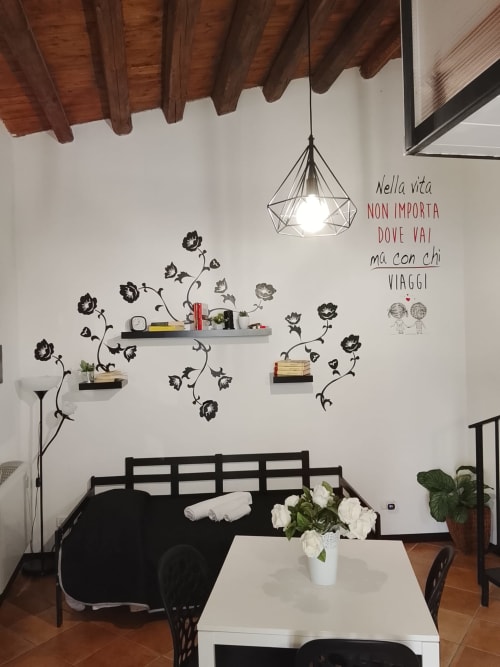 Appartamento Bianco a Case Vacanze Borgo i Stritti con divano nero, tavolo bianco, decorazioni floreali e soffitto con travi in legno