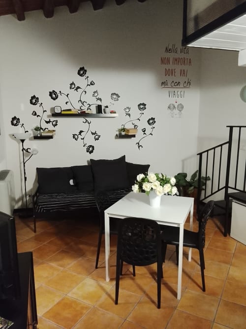 Zona soggiorno moderna con divano nero, tavolo bianco e arte floreale a Case Vacanze Borgo i Stritti a Petralia