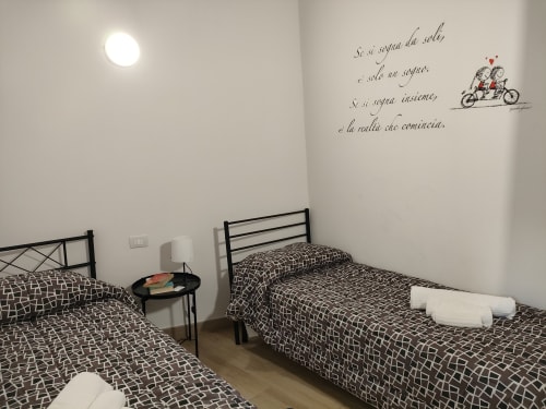 Camera da letto con due letti in ferro battuto, trapunte decorate, opere d'arte murale in italiano e tavolino rotondo a Case Vacanze Borgo i