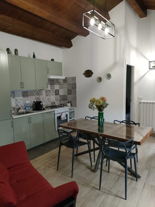 Cucina e zona pranzo moderna di Case Vacanze Borgo i Stritti con mobili verdi, travi in legno e fiori in terracotta