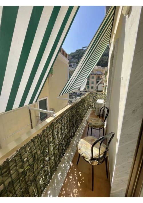 Balcone di Casa Ida a Vietri sul Mare con tenda a righe verdi, vista sulla città e sedie nere