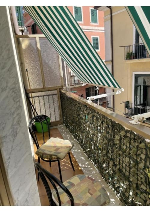Balcone stretto di Casa Ida 2 a Vietri sul Mare con tenda a righe verdi, edifici colorati, sedute e vista sulla città