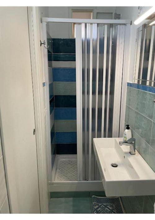 Bagno moderno dell'appartamento Casa Ida a Vietri sul Mare, con lavabo bianco, tenda doccia a righe e pareti piastrellate