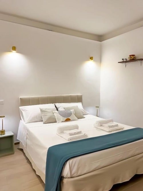 Camera moderna alla Casa Ida B&B di Vietri con testata beige, biancheria bianca, passatoia turchese e applique in ottone