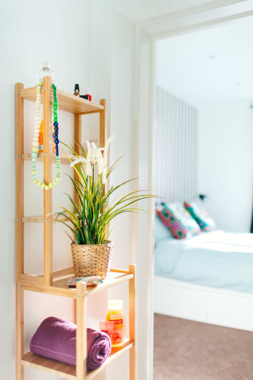 Étagère en bois dans la chambre de B&B Place Jourdan Bruxelles avec plante en pot, colliers de perles, serviette et articles de toilette