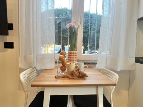 Luminosa sala da pranzo nell'appartamento di Lipomo con tavolo in legno, sedie bianche, fiori freschi e servizio caffè con vista sul giardino