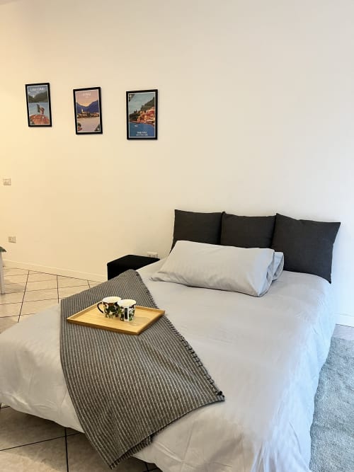 Camera moderna a Le case di Angy con biancheria bianca, cuscini neri, vassoio in legno con tazze, plaid a righe e tre quadri