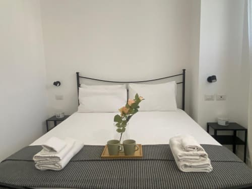 Camera moderna presso Le case di Angy con letto in ferro nero, biancheria bianca, fiori decorativi e servizi ad Albese Con