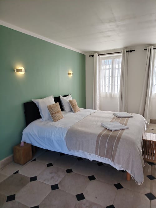 Chambre moderne au Domaine Chapelle avec mur d'accent vert sauge, literie blanche et vue sur le jardin à travers des rideaux voilage