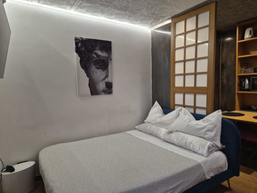 Camera moderna nell'appartamento Nidus di Giulia a Babaja Roma con letto, cuscini bianchi, scultura astratta e scaffali in legno