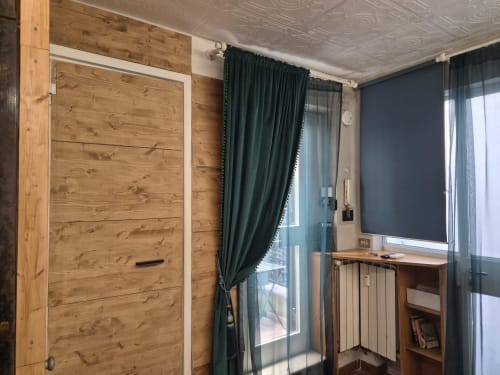 Camera da letto moderna in appartamento romano con armadio in legno, tende verdi, scrivania, termosifone e balcone con vista sulla città