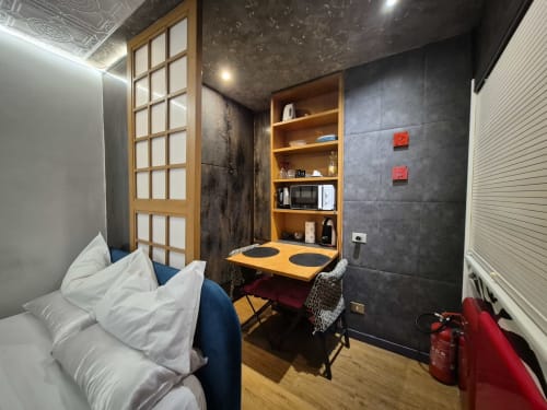 Monolocale moderno a Roma con letto, scrivania in legno, ripiani angolo cottura, piastrelle scure e arredi contemporanei
