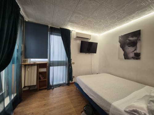 Camera moderna nell'appartamento Nidus di Giulia a Roma, con letto, scrivania, TV a schermo piatto e balcone con vista sulla città