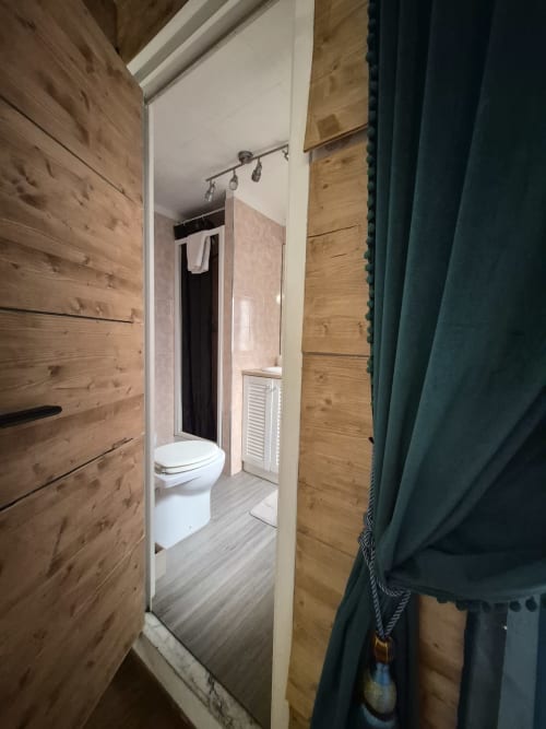 Bagno dell'appartamento Nidus di Giulia presso Babaja, Roma. Toilet bianco, pareti in legno, pavimento piastrellato, doccia scura