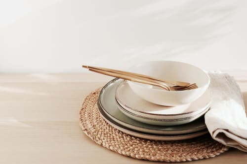 Mise en place élégante avec assiettes empilées, baguettes en bois et serviette lin sur napperon tissé à La Grange Aux