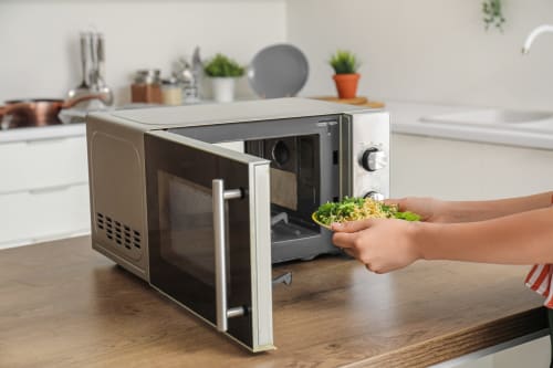 Hôte préparant une salade fraîche au micro-ondes moderne dans la cuisine de La Grange Aux Etangs, gîte à Sennely, France
