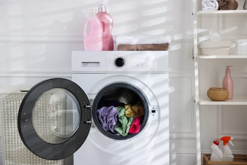 Buanderie moderne à La Grange Aux Etangs avec lave-linge blanc, vêtements colorés, détergent rose et bien organisée
