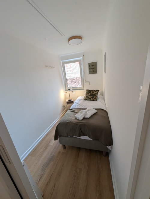 Narrow bedroom in Bi d'Tante Irène cottage at Bi d'Grosseltere BnB, Kirrwiller, with single bed, window view, and minimalist