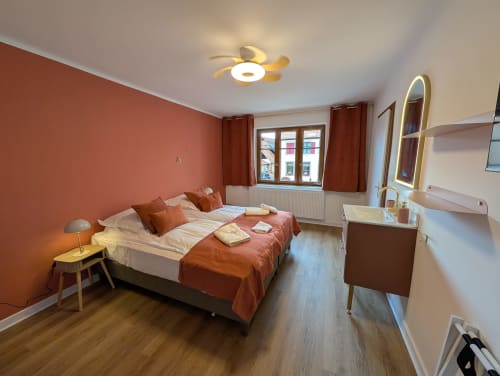Modern bedroom with terracotta accent wall, queen bed with rust bedding, wooden floor, and garden view window at Bi