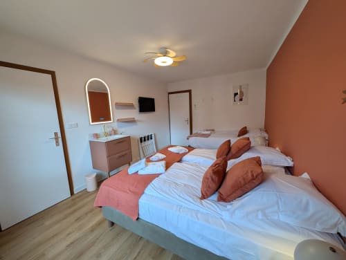 Bright cottage bedroom at Bi d'Grosseltere with two beds, terracotta accent wall, vanity with mirror, and modern amenities in