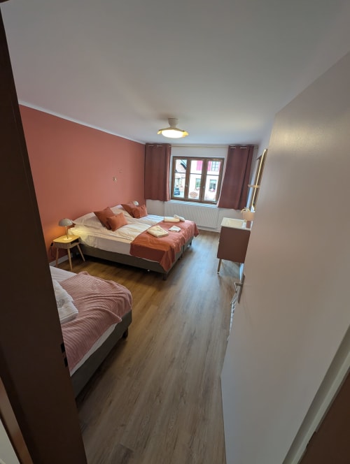 Spacious cottage bedroom at Bi d'Grosseltere with twin beds, coral accent wall, garden view windows, and modern amenities in