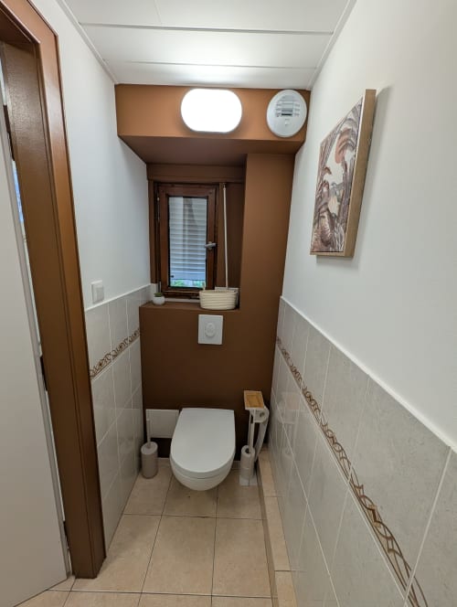 Modern bathroom in Bi d'Tante Irène cottage at Bi d'Grosseltere B&B, Kirrwiller, with white toilet, beige tiles, and brown