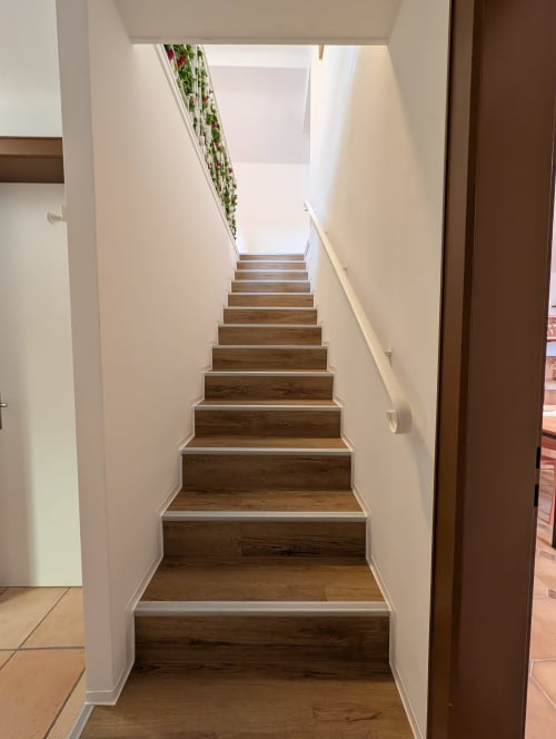 Wooden staircase with white walls leading upstairs in Bi d'Grosseltere cottage, Kirrwiller