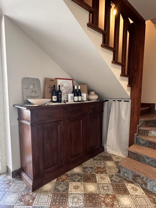 Credenza in legno scuro con bottiglie di vino e decorazioni sotto il soffitto mansardato al Casale Rusignûl, Cassegliano