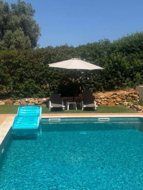 Crystal blue private pool with float, white umbrella, loungers, and lush green surroundings at Villa Tulipa, Lagoa