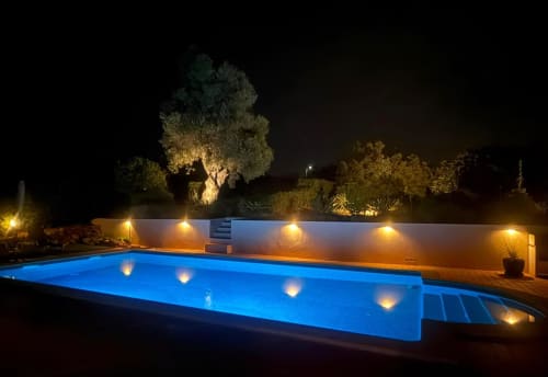 Illuminated swimming pool at night with blue water, lounge chairs, and lit white wall at Villa Tulipa in Lagoa