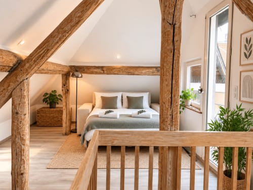 Chambre loft rustique à Metz avec poutres apparentes, lit queen-size, balustrades bois et vue sur la ville