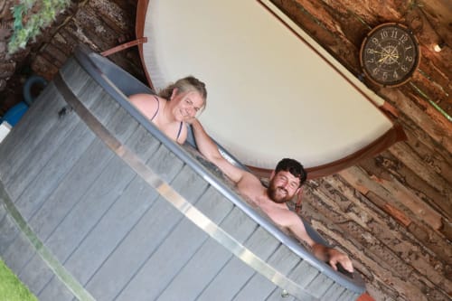 Two guests enjoying a hot tub at Greenvale Cabins in Newry with rustic wooden decor and vintage clock.