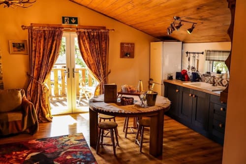 Warm orange cabin interior at Greenvale Cabins with round table, kitchenette, balcony doors, and mountain views in Newry