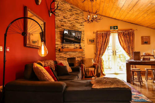 Cozy sitting area at Greenvale Cabins with red and orange walls, black sofa, fireplace, TV, and mountain views in Newry