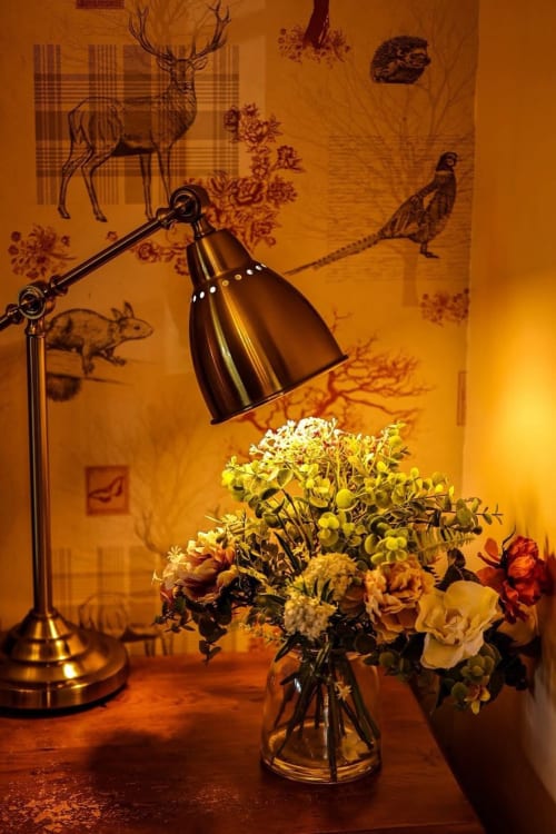 Warm ambient lighting illuminates wildflowers in a vase with adjustable desk lamp at Greenvale Cabins Colorado Apartment in
