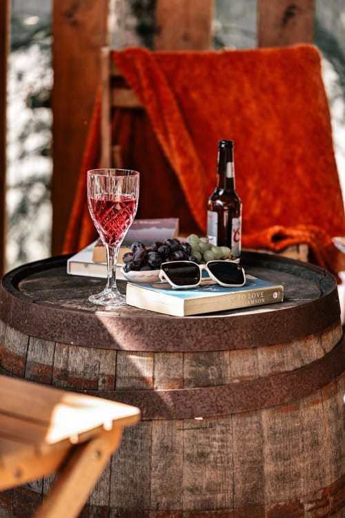 Wine, grapes, and sunglasses on wooden barrel table at Greenvale Cabins mountain view apartment in Newry