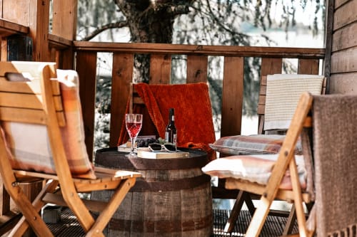 Wooden deck seating at Greenvale Cabins with wine glass, bottle, and mountain views through pine trees in Newry