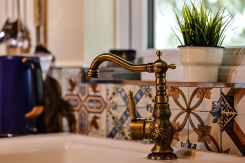 Ornate brass faucet at sink in Colorado Apartment at Greenvale Cabins, Newry, with decorative tile backsplash and potted