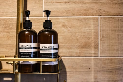 Dark amber pump bottles of shampoo and body wash on brass shelf in Greenvale Cabins bathroom, Newry
