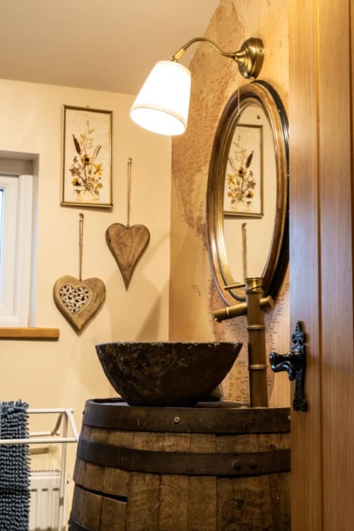 Rustic bathroom sink at Greenvale Cabins with barrel base, bronze mirror, wall sconce, and decorative heart ornaments
