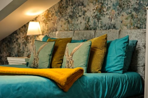 Cozy sitting area at Greenvale Cabins with teal sofa, decorative pillows featuring hares, mustard throw, and textured wall