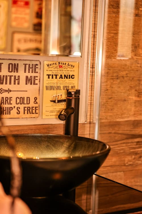 Black vessel sink with vintage Titanic White Star Line poster and wooden fixtures in Greenvale Cabins bathroom