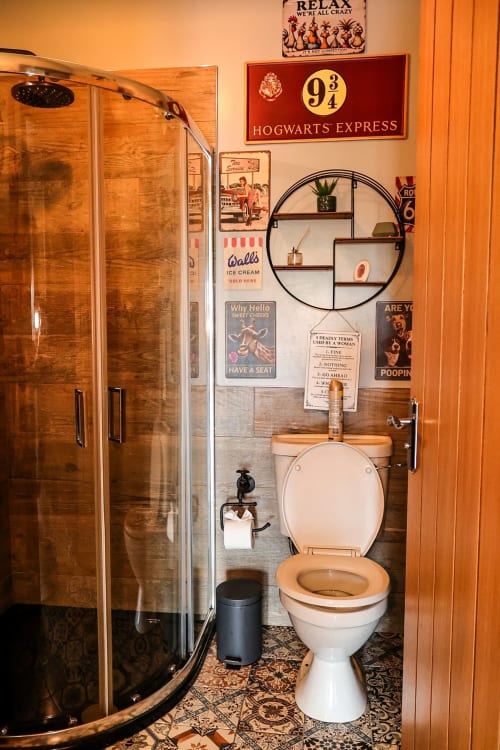 Themed bathroom at Greenvale Cabins with shower, toilet, circular mirror shelf, and vintage Harry Potter and retro decor