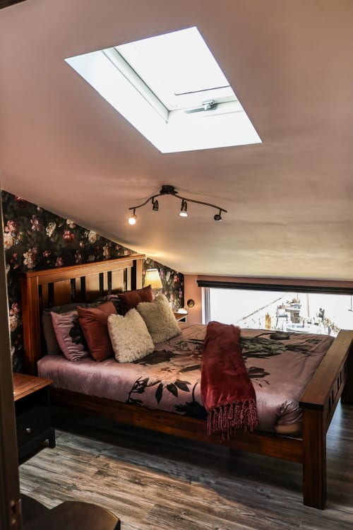 Cozy attic bedroom at Greenvale Cabins with wooden bed, floral wallpaper, skylights, and mountain views from balcony in Newry